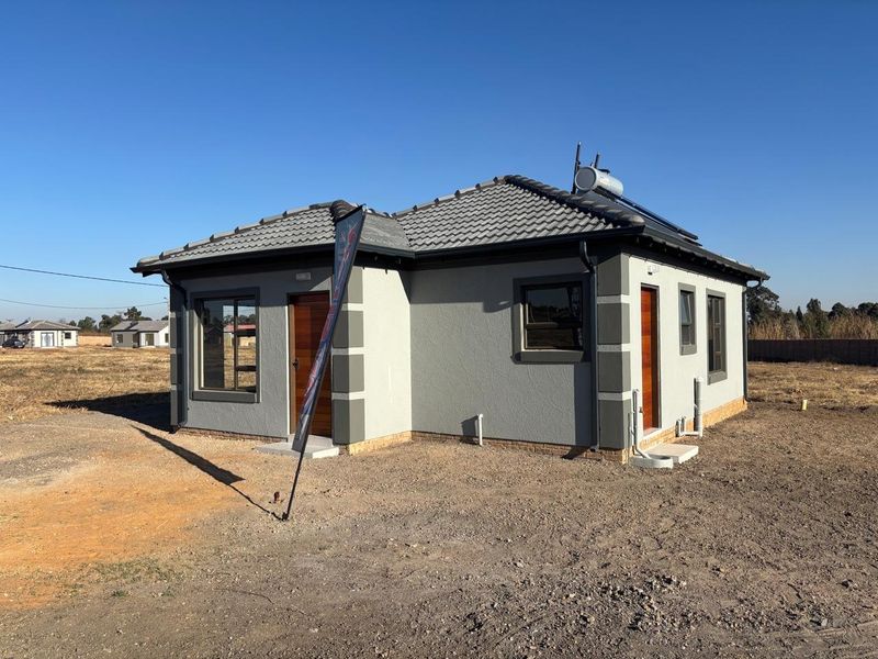 A modern single-story detached house featuring a tiled roof, solar geyser, and contemporary grey exterior finish with timber doors.