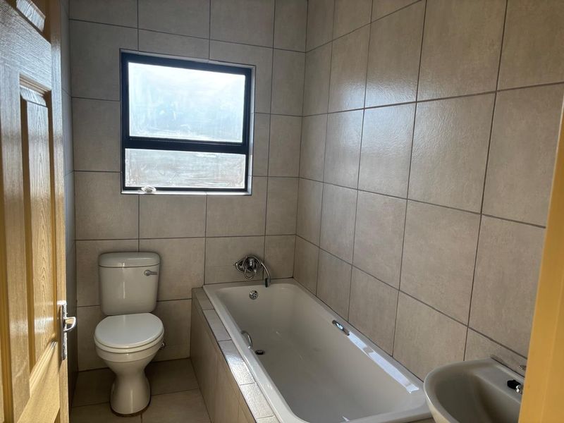 A functional bathroom featuring a built-in bathtub, pedestal basin, and toilet, finished with neutral ceramic wall and floor tiles.
