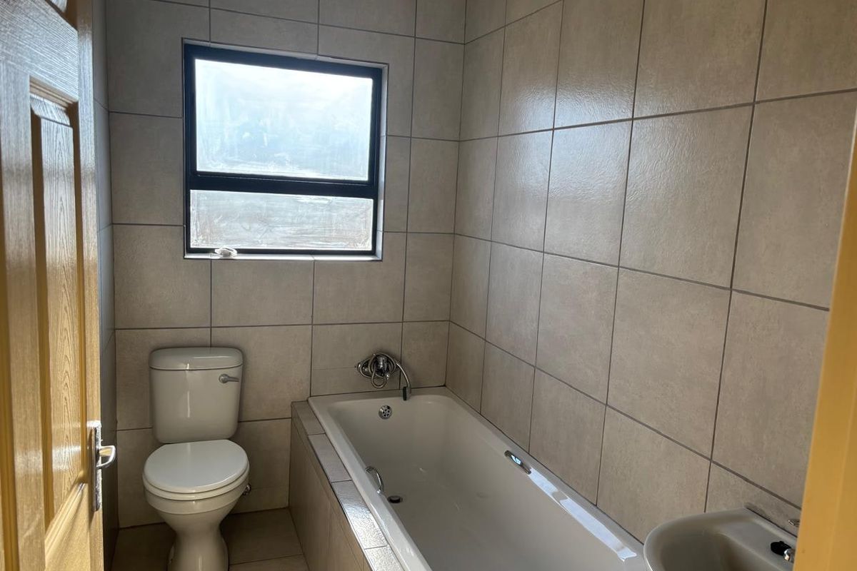 A functional bathroom featuring a built-in bathtub, pedestal basin, and toilet, finished with neutral ceramic wall and floor tiles.