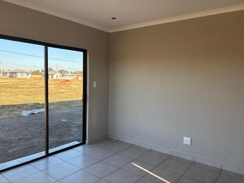 A bright, empty living area featuring neutral wall finishes, ceramic floor tiles, and a large sliding glass door providing access to the exterior.