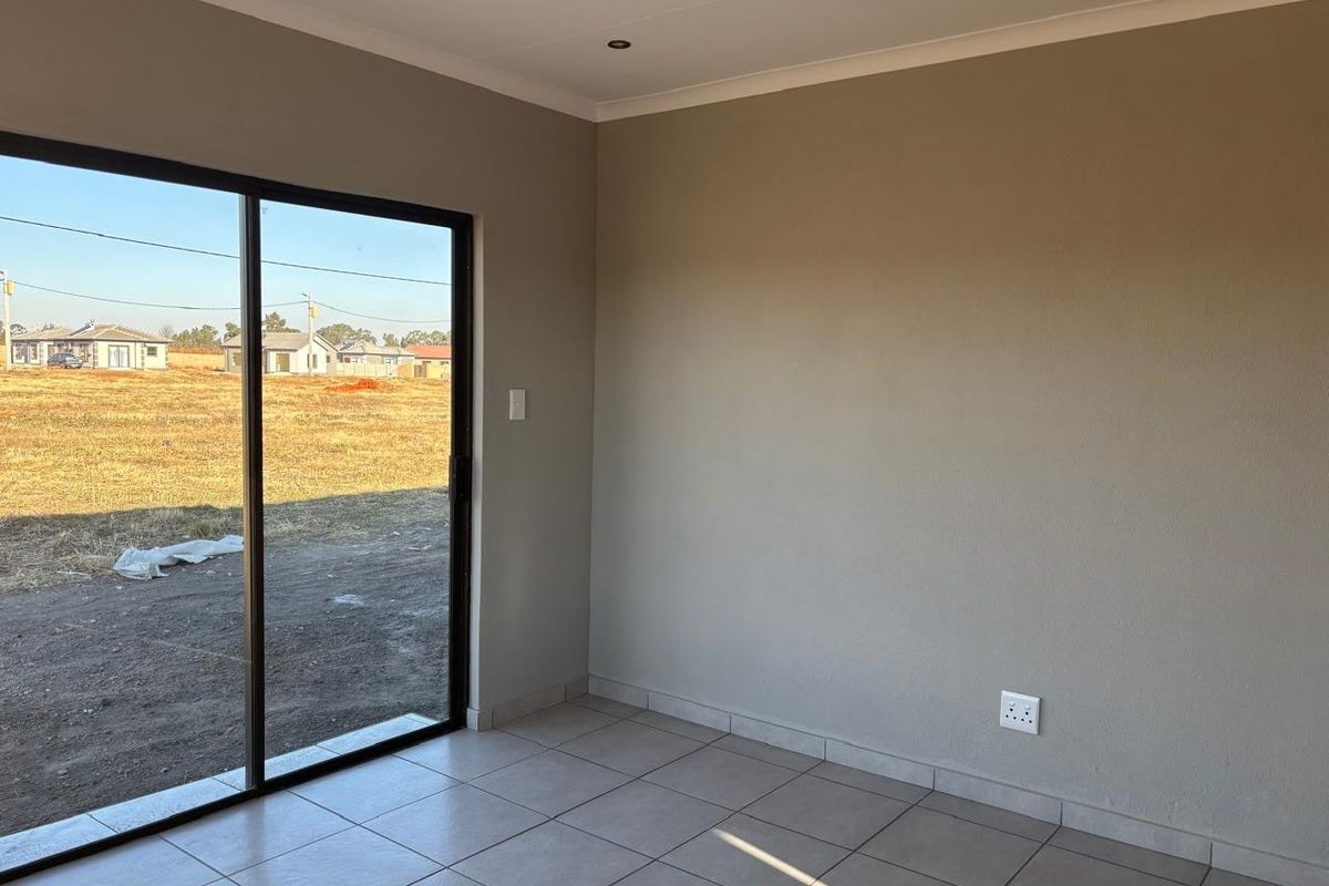 A bright, empty living area featuring neutral wall finishes, ceramic floor tiles, and a large sliding glass door providing access to the exterior.