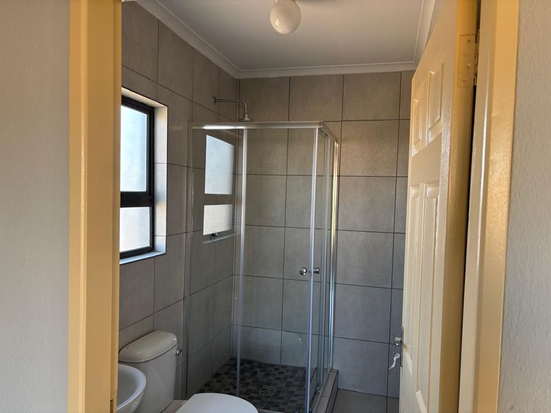 A clean and functional bathroom featuring a glass shower enclosure, tiled walls, and a standard toilet.