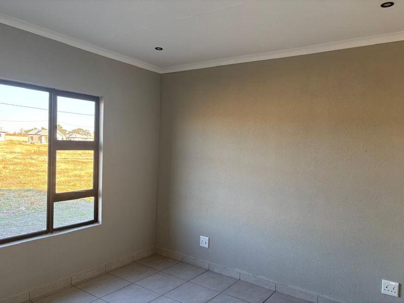 A clean, empty bedroom featuring neutral wall paint, tiled flooring, and recessed downlights, offering a blank canvas for personalization.