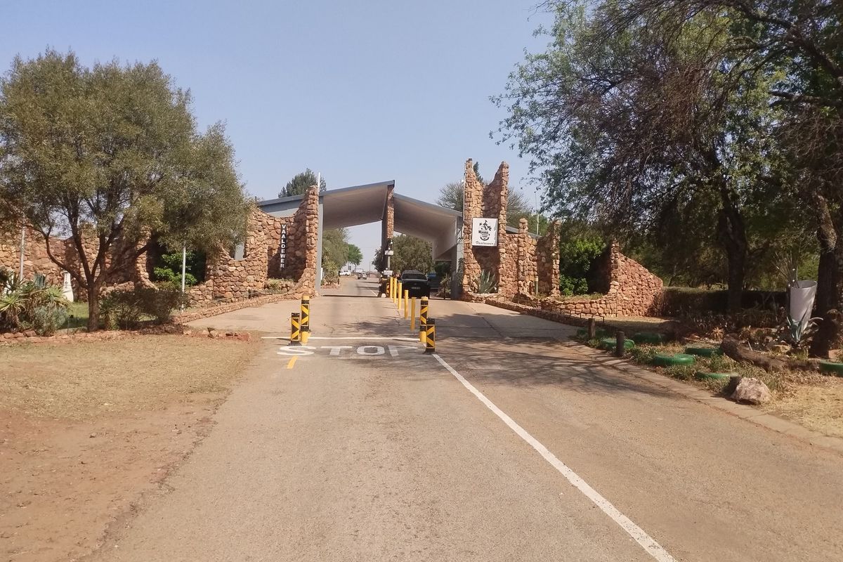 Entrance view of the residential estate featuring a stone masonry gatehouse, security access point, and paved driveway.
