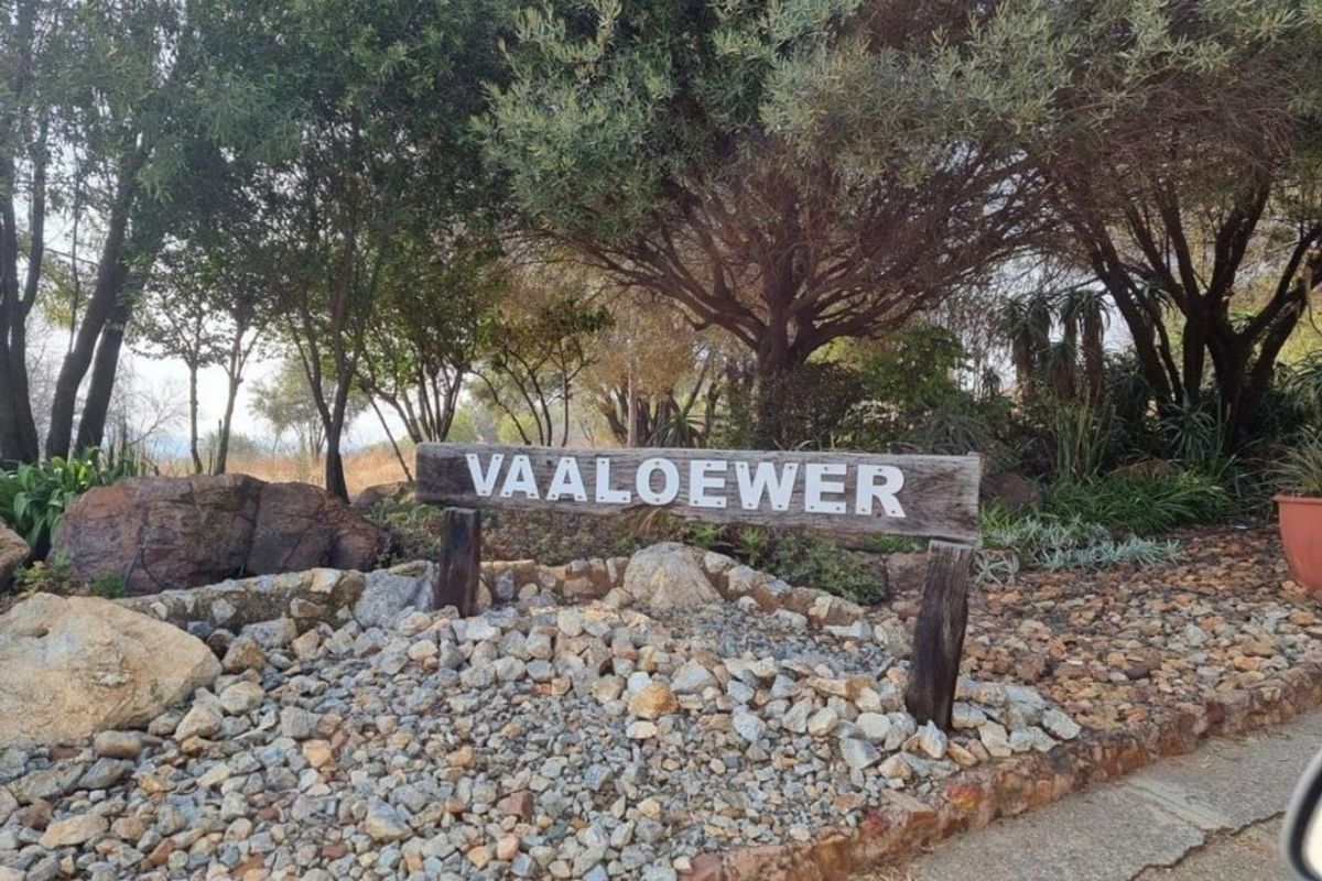 A view of the Vaaloewer entrance sign featuring a stone retaining wall and mature trees in a landscaped garden setting.