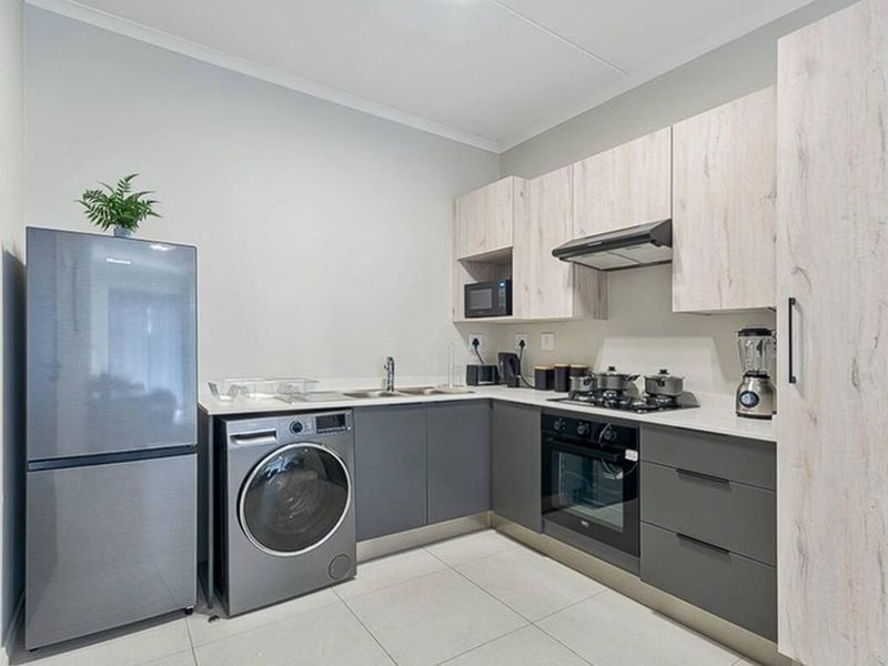 Modern kitchen featuring sleek grey and light wood cabinetry, integrated appliances, gas hob, and durable tiled flooring in a compact, functional layout.