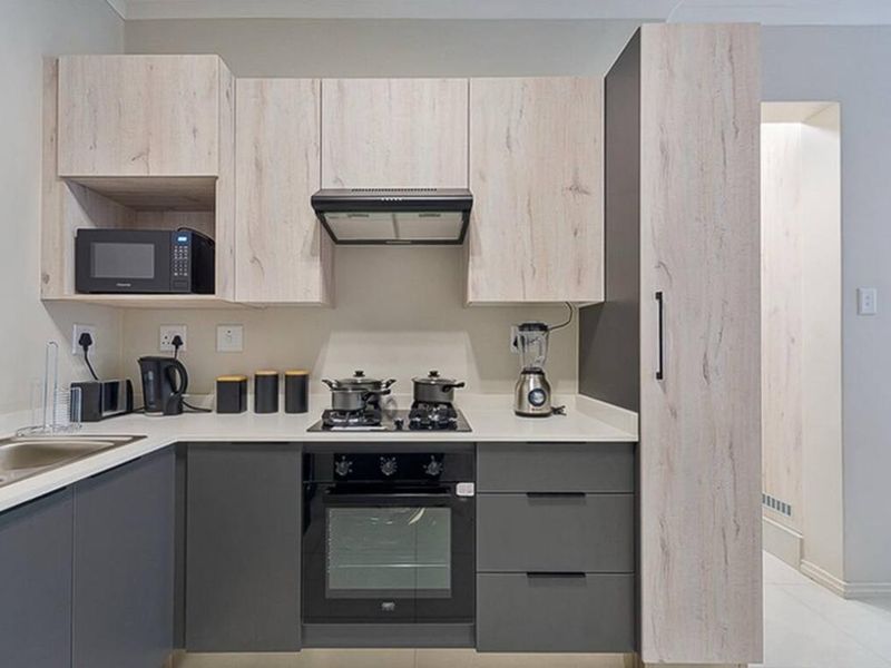 Modern kitchen featuring sleek grey and light wood-grain cabinetry, stone countertops, integrated oven, gas hob, and built-in microwave.