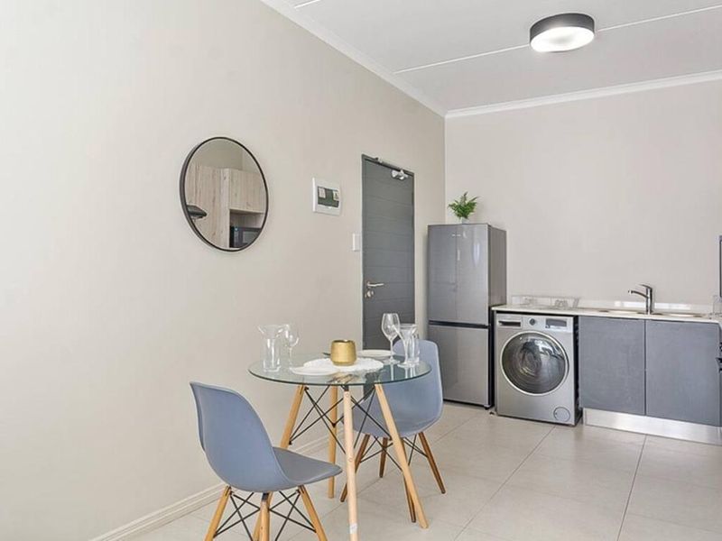 A compact open-plan living area featuring a modern kitchenette with built-in cabinetry, stainless steel sink, and tiled flooring throughout.