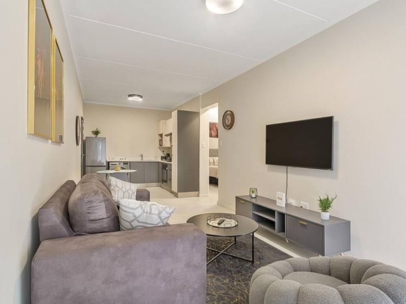 An open-plan living area featuring a compact kitchen with built-in cabinetry and tiled flooring, seamlessly connected to the lounge space.