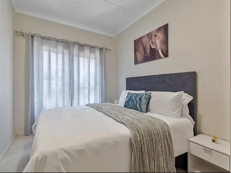 A well-maintained bedroom featuring neutral wall tones, tiled flooring, and a large window with installed curtain rods.