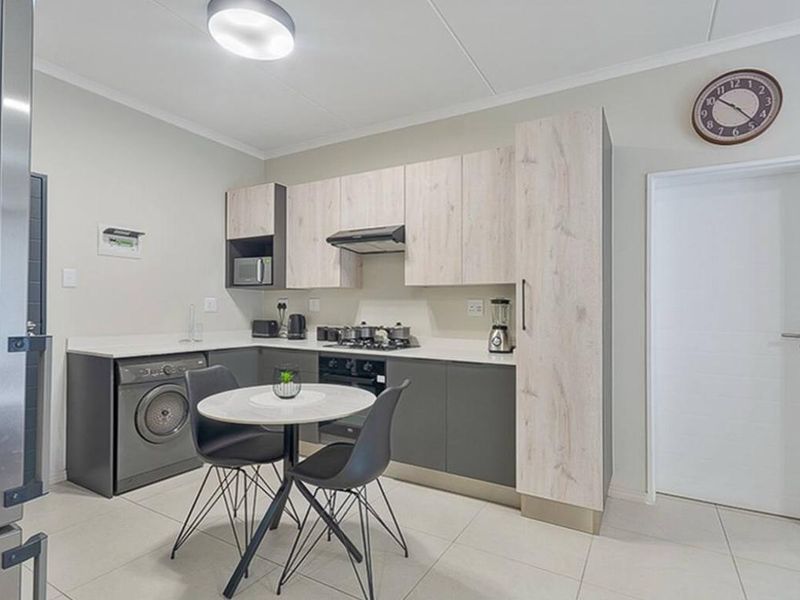 Modern kitchen featuring two-tone cabinetry, stone countertops, integrated gas hob, extractor fan, and built-in oven with space for a washing machine.