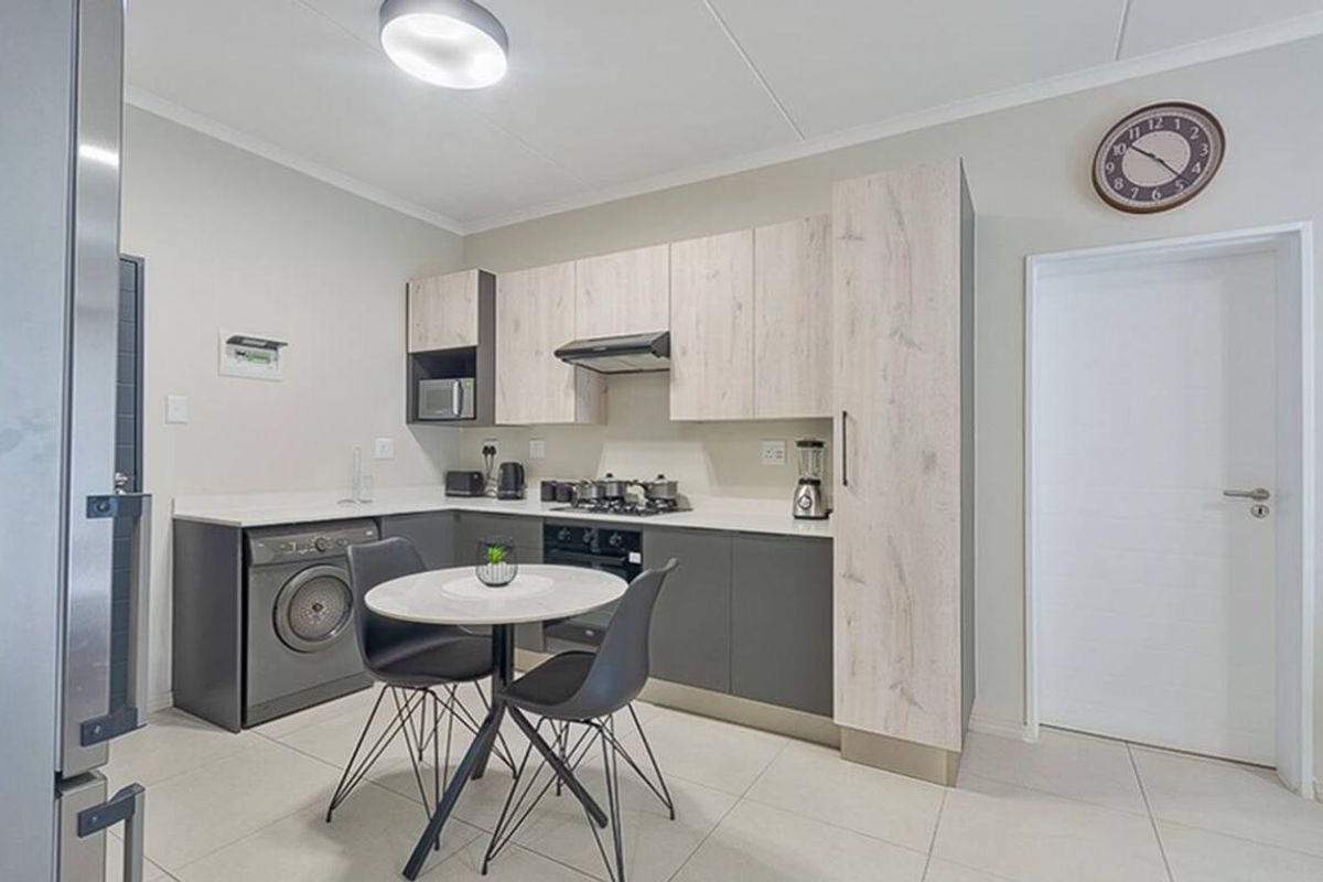 Modern kitchen featuring two-tone cabinetry, stone countertops, integrated gas hob, extractor fan, and built-in oven with space for a washing machine.