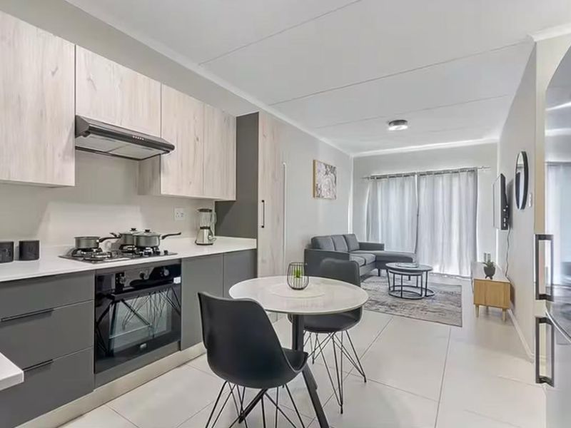 Modern open-plan apartment featuring a contemporary kitchen with built-in cabinetry, gas hob, and oven, flowing into a bright living area with sliding door access.