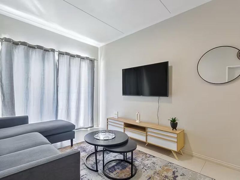 A well-maintained living room featuring neutral wall tones, tiled flooring, and large windows with curtain treatments.