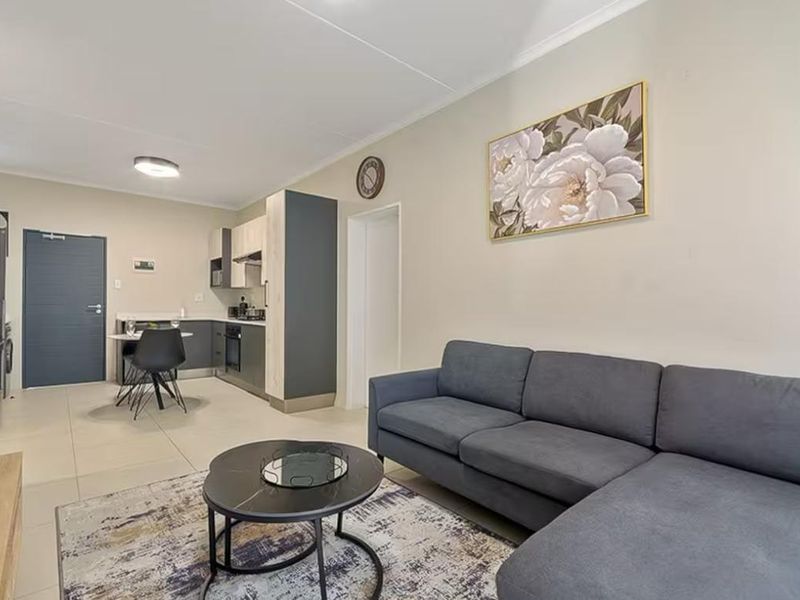 Modern open-plan living area featuring a sleek kitchen with built-in cabinetry, integrated appliances, and neutral tiled flooring throughout.