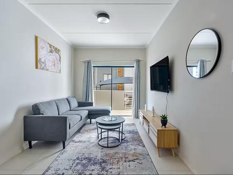 A well-maintained living room featuring neutral tiled flooring, clean wall finishes, and a sliding glass door providing access to an outdoor balcony area.