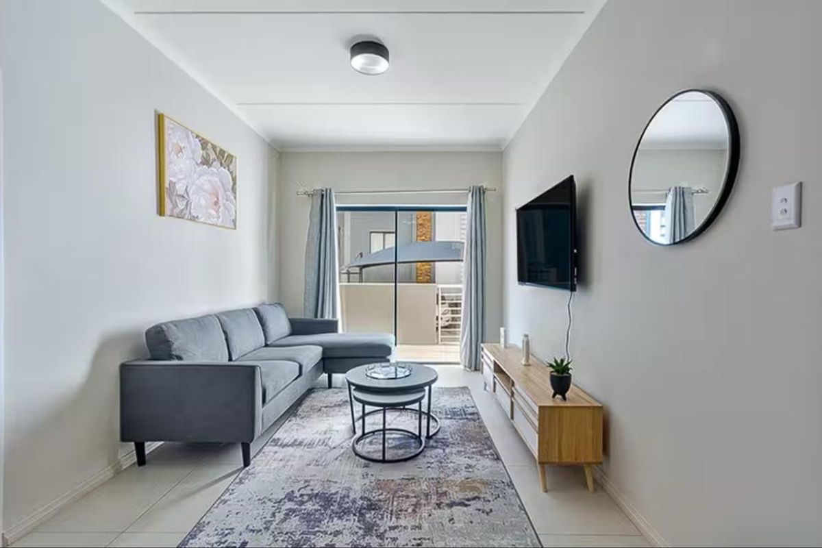 A well-maintained living room featuring neutral tiled flooring, clean wall finishes, and a sliding glass door providing access to an outdoor balcony area.