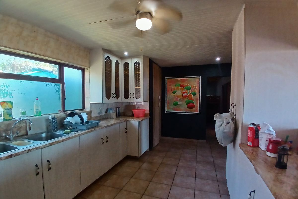 A functional kitchen featuring laminate cabinetry, double basin sink, tiled flooring, and a ceiling fan, offering a dated but practical layout.