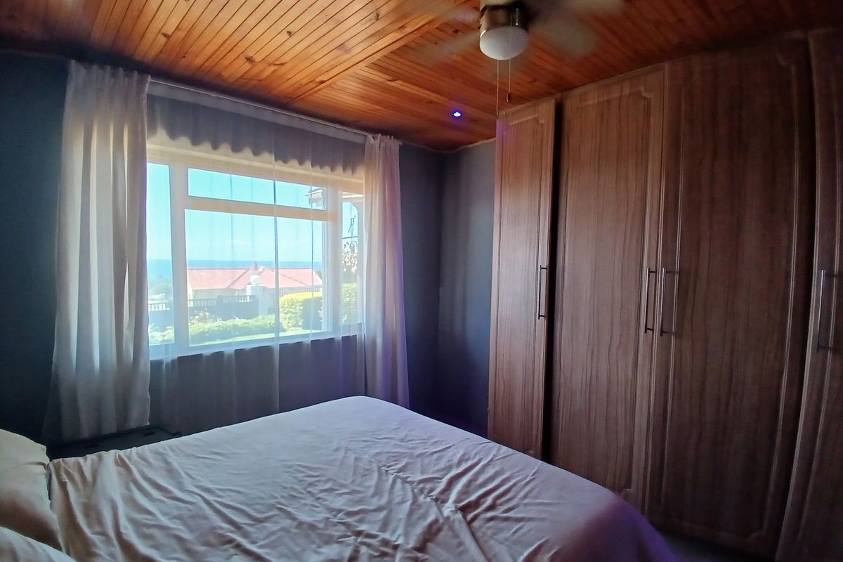 A cozy bedroom featuring a warm timber-clad ceiling, ceiling fan, and extensive built-in wooden cupboards, offering ample storage and a pleasant view.