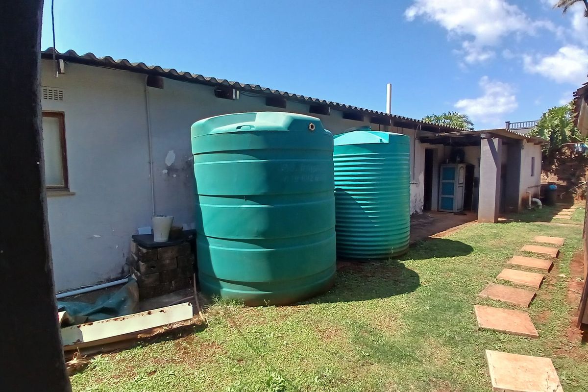 Rear exterior view of the property featuring two large water storage tanks, a corrugated roof, and a grassed yard with concrete stepping stones.
