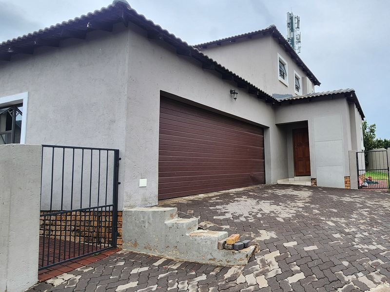 Front elevation of a double-story house featuring a double garage, paved driveway, and secure gated entrance.