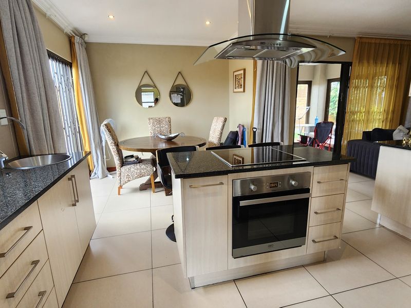 Open-plan kitchen and dining area featuring a central island with built-in oven, electric cooktop, granite countertops, and modern tiled flooring.