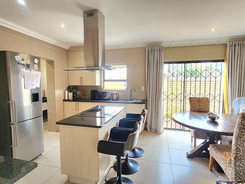 Open-plan kitchen and dining area featuring a central island with hob, modern cabinetry, and direct access to the outdoor patio through a sliding door.