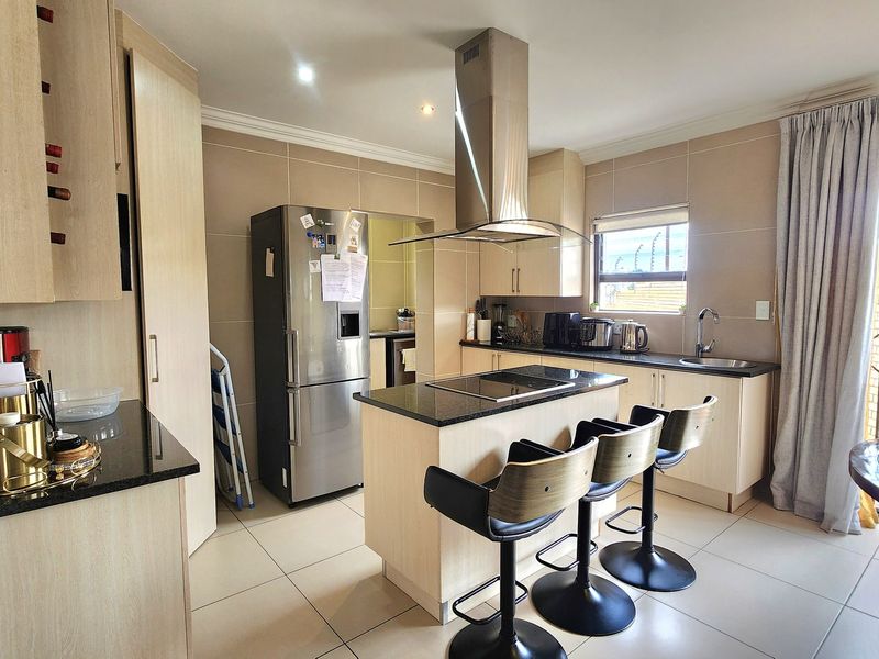 Modern kitchen featuring a central island with a built-in cooktop, granite countertops, ample cabinetry, and tiled flooring, offering a functional and contemporary cooking space.