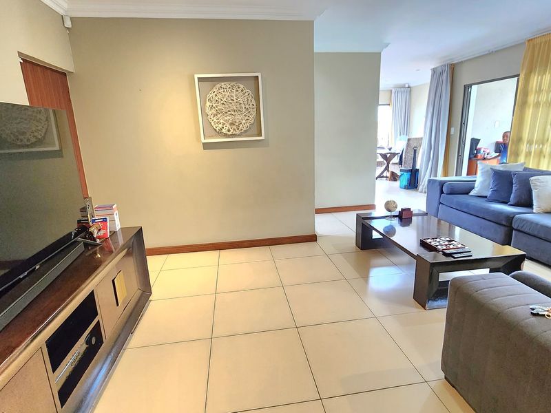 Spacious living room featuring neutral tiled flooring, cove cornicing, and direct access to an adjoining area through a sliding door with security gate.