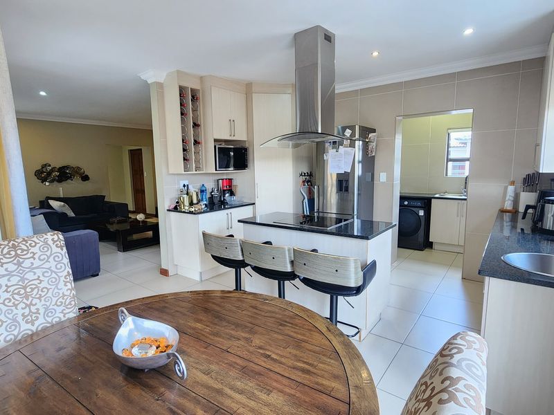 Open-plan kitchen featuring a central island with breakfast bar, granite countertops, modern cabinetry, and an adjoining scullery area.