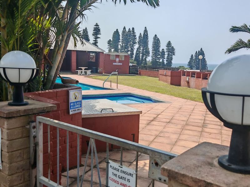 Communal pool area featuring a paved deck, brick boundary walls, and a secure gated entrance, set within a landscaped complex.