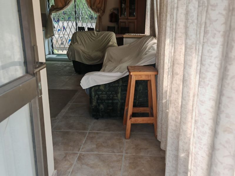 A living area featuring tiled flooring, a vaulted ceiling with a fan, and access to an outdoor space through a security gate.