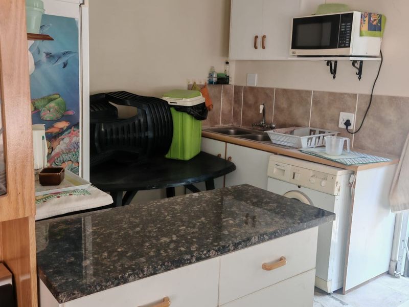 A functional scullery area featuring built-in cabinetry, granite countertops, a double sink, and tiled backsplash, providing practical utility space for the home.