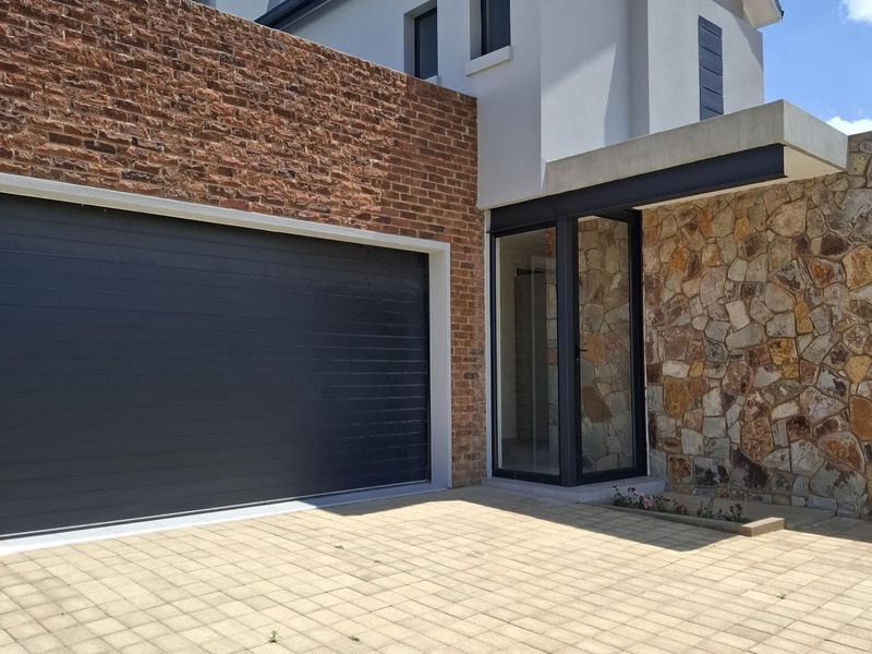 Modern architectural facade featuring a combination of face brick, natural stone cladding, and a double garage with a paved driveway.