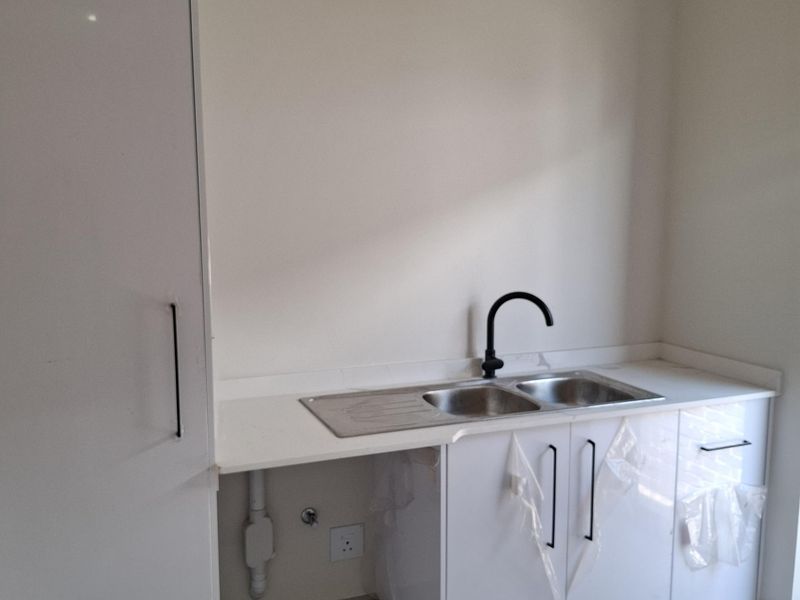 A modern laundry area featuring white cabinetry, a stainless steel double sink, and a sleek black faucet, with plumbing connections for appliances.