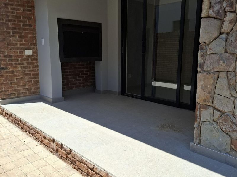 Covered patio area featuring a built-in braai, stone cladding accents, and large sliding glass doors leading into the home.