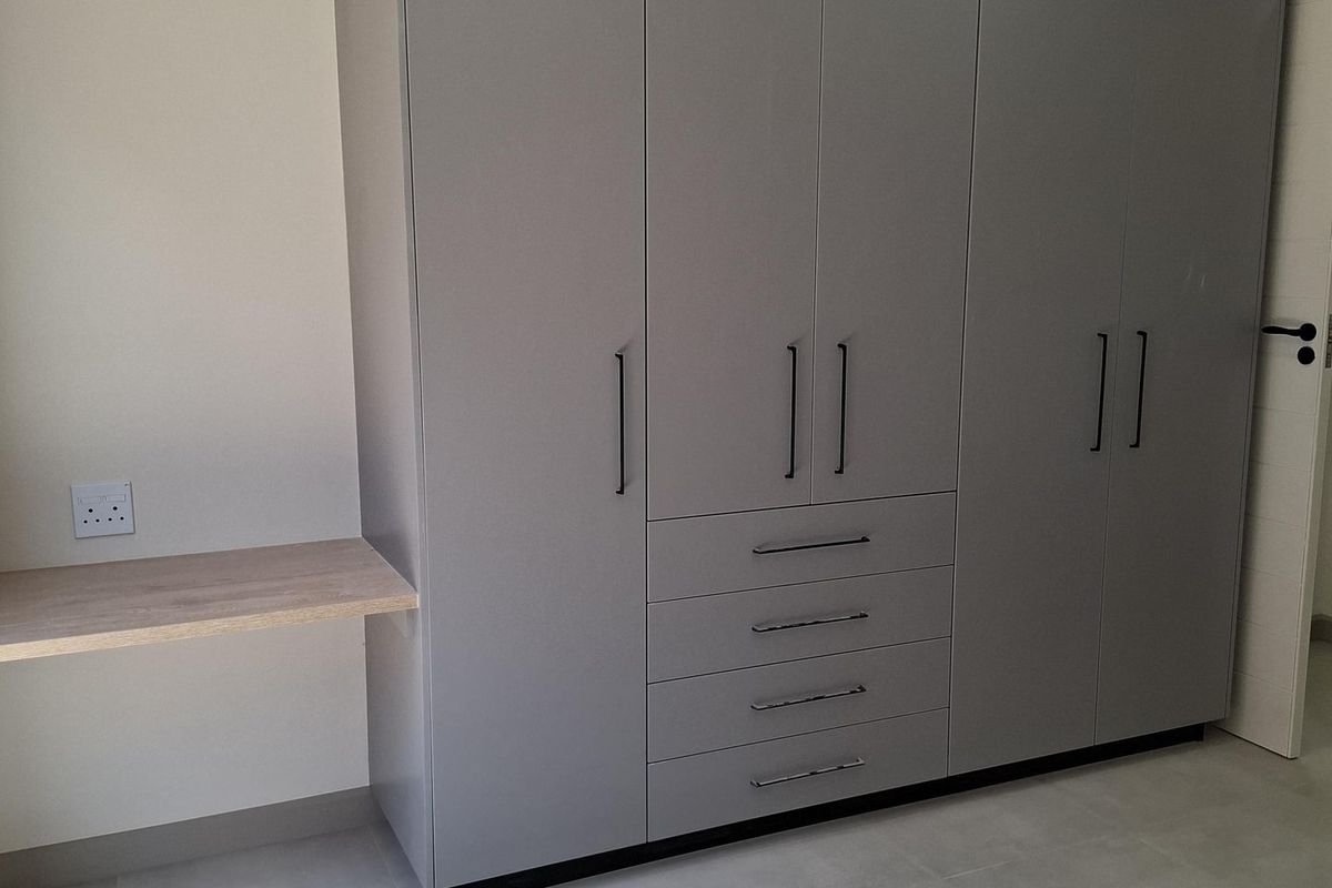 A modern bedroom featuring built-in grey cabinetry with integrated drawers and a floating wooden desk shelf.