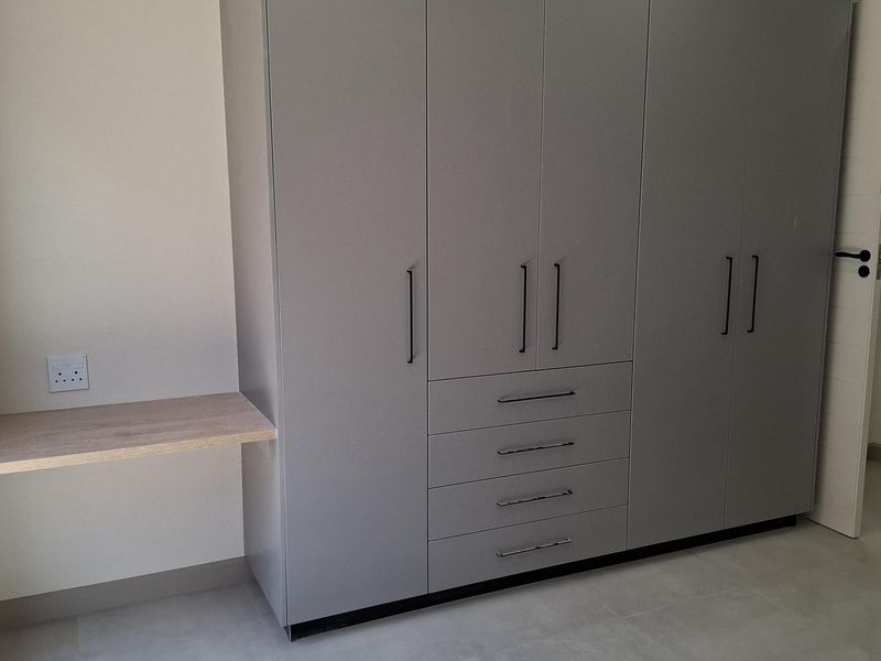 A modern bedroom featuring built-in grey cabinetry with integrated drawers and a floating wooden desk shelf.
