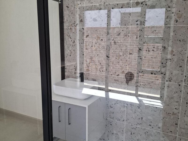 Modern bathroom featuring a walk-in shower with terrazzo-style wall tiling, a sleek vanity cabinet with a vessel sink, and black framed glass shower screen.