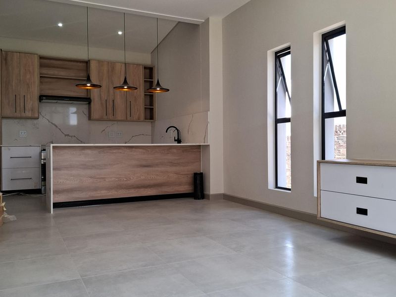 Modern open-plan kitchen and living area featuring light wood cabinetry, stone-look backsplash, sleek black fixtures, and large format floor tiles.