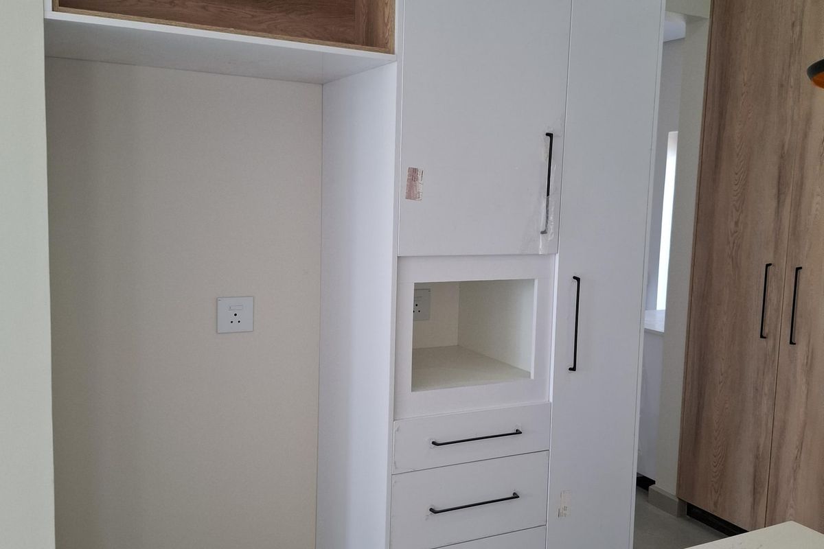 Modern kitchen cabinetry featuring high-gloss white finish, integrated shelving, and stone-look countertop, providing clean lines and functional storage space.