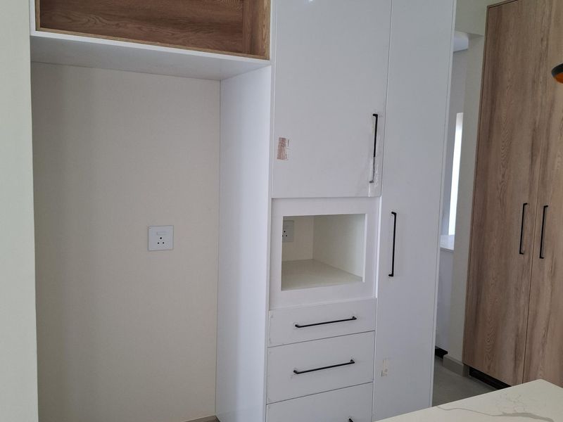Modern kitchen cabinetry featuring high-gloss white finish, integrated shelving, and stone-look countertop, providing clean lines and functional storage space.