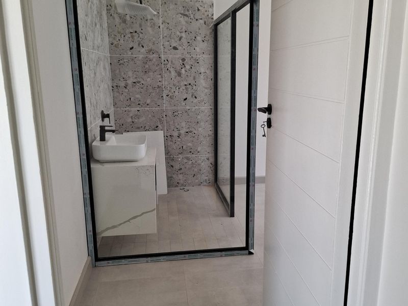 Modern bathroom featuring a walk-in shower with black frame, terrazzo-style wall tiles, floating vanity with vessel sink, and large format floor tiles.