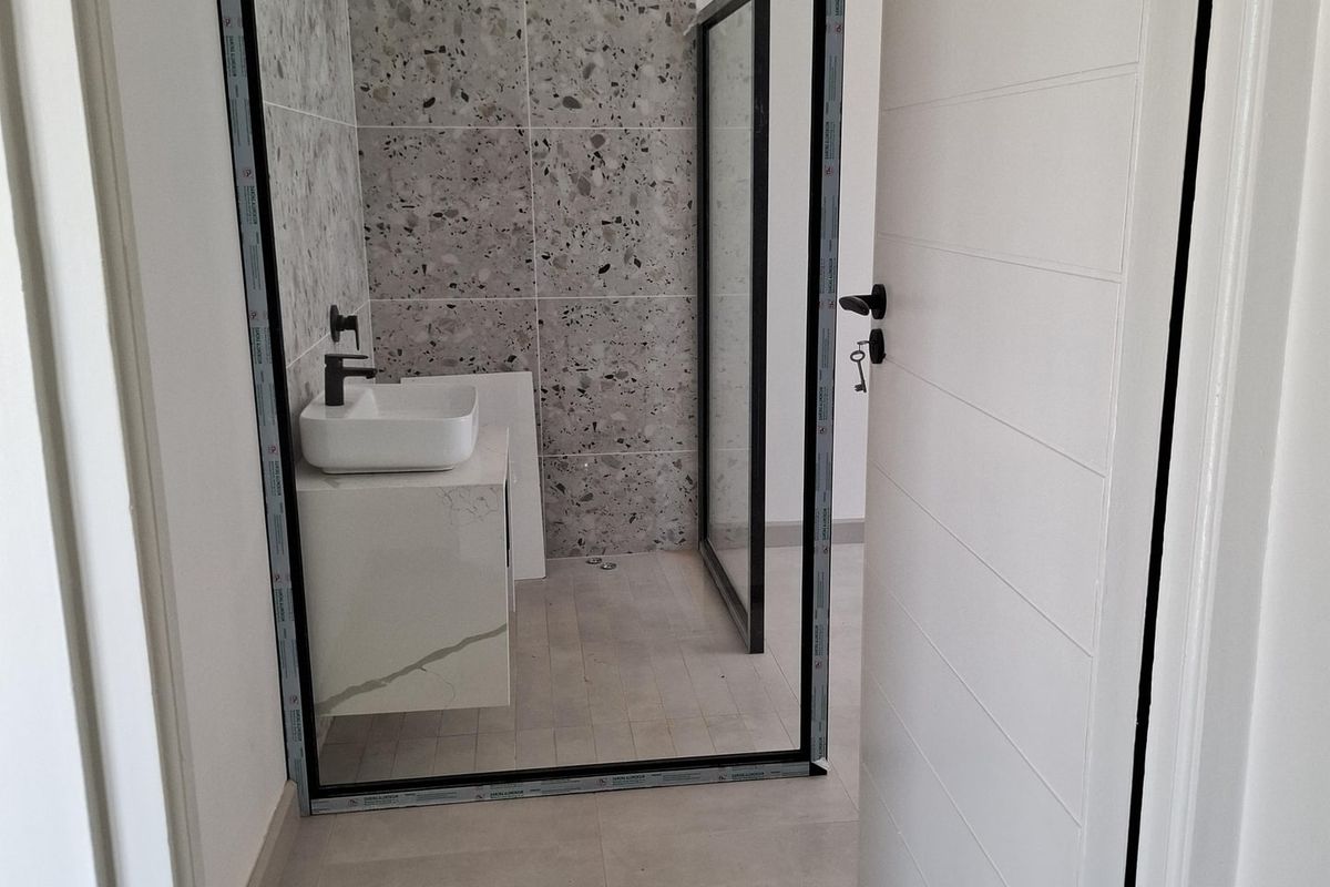Modern bathroom featuring a walk-in shower with black frame, terrazzo-style wall tiles, floating vanity with vessel sink, and large format floor tiles.