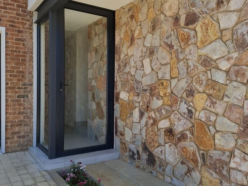 Modern entrance featuring a glass door, natural stone cladding, and a built-in concrete planter box.