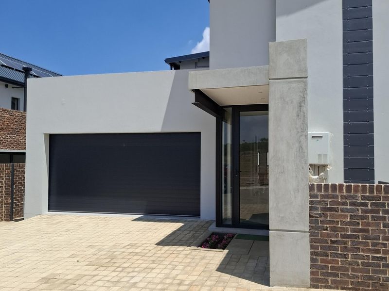 Modern front facade featuring a paved driveway, double garage, and a contemporary entrance with concrete architectural detailing and brick accents.