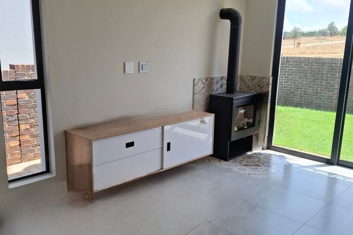 Modern living room featuring a sleek freestanding fireplace, air conditioning unit, large sliding glass doors, and neutral tiled flooring.