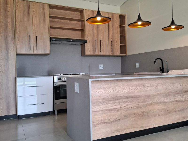 Modern kitchen featuring wood-grain cabinetry, stone-look countertops, a central island, and contemporary pendant lighting in a clean, open-plan layout.
