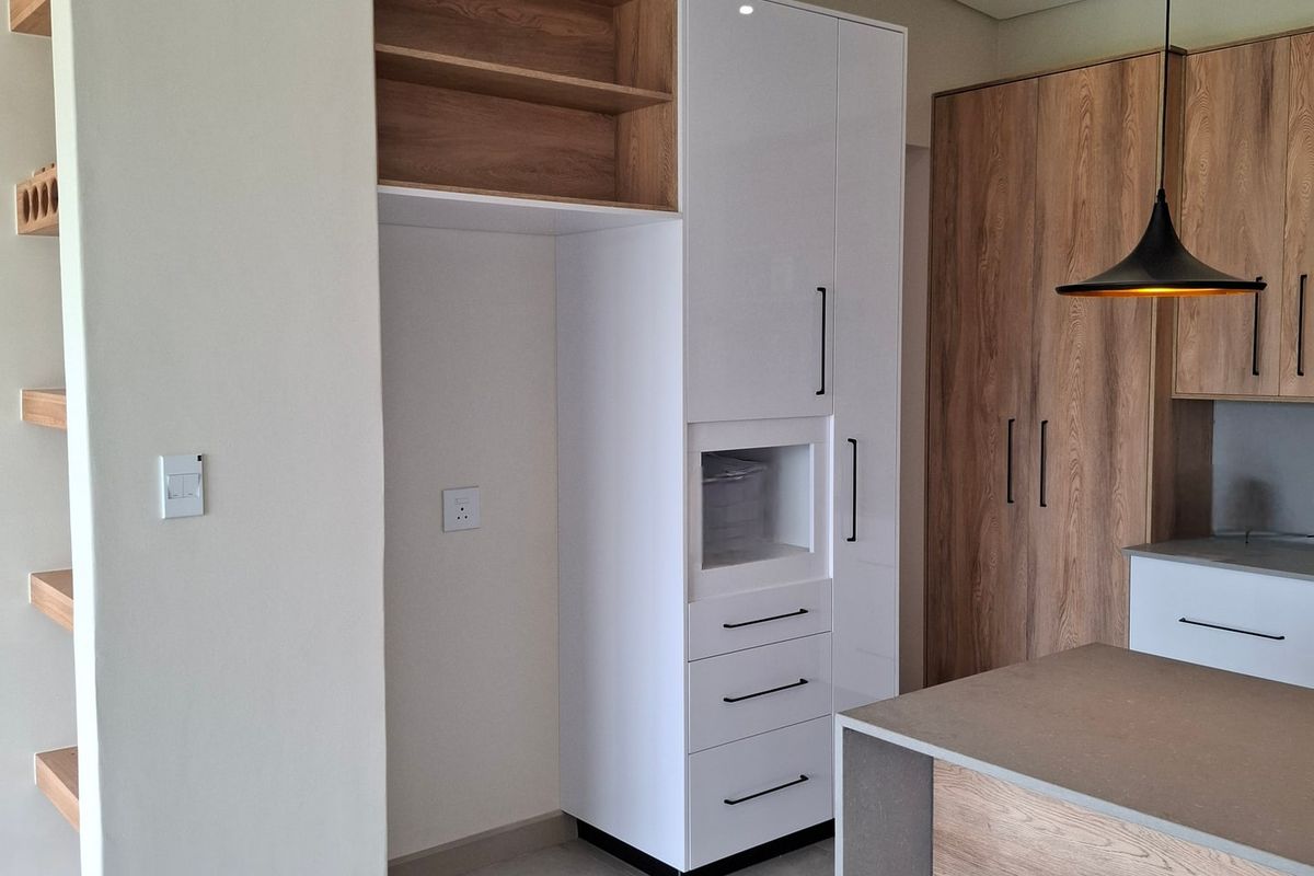 Modern kitchen featuring sleek two-tone cabinetry, a central island with stone countertop, and contemporary pendant lighting in a clean, minimalist space.