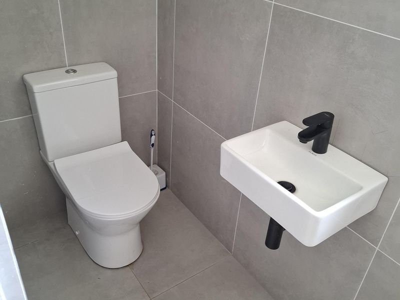 A modern, minimalist guest bathroom featuring large-format grey porcelain tiles, a wall-mounted basin with a black mixer tap, and a contemporary toilet.